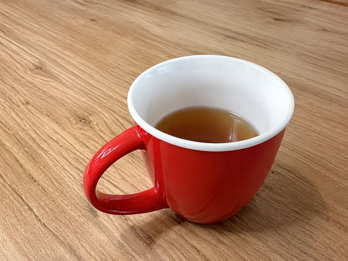 Red mug containing chicken bone broth on a timber table. 